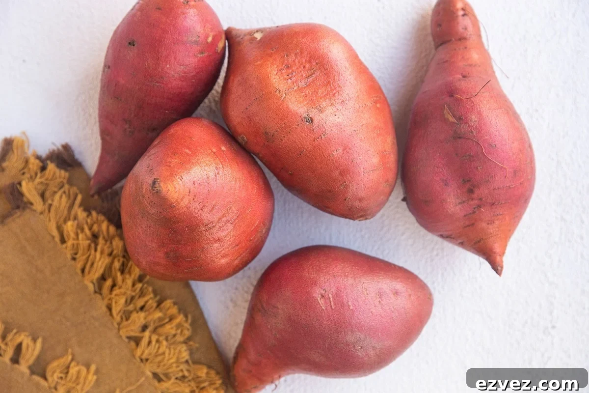 Raw sweet potatoes on a white background with a golden napkin to the side.