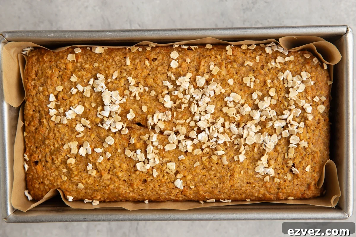 Loaf pan lined with parchment paper with sweet potato bread inside, sprinkled with oats, fresh out of the oven.
