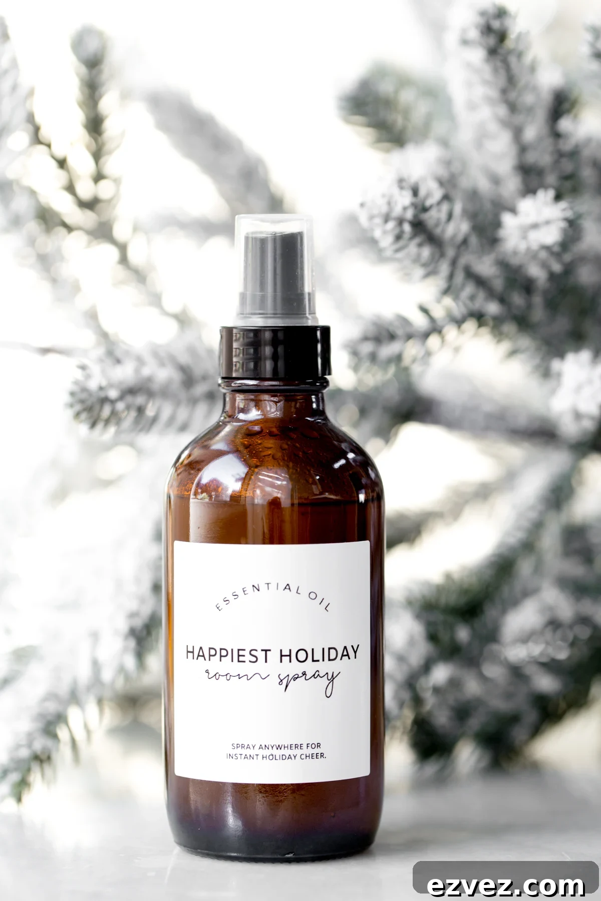 Homemade essential oil Christmas room spray on marble with snow covered tree branches in the background