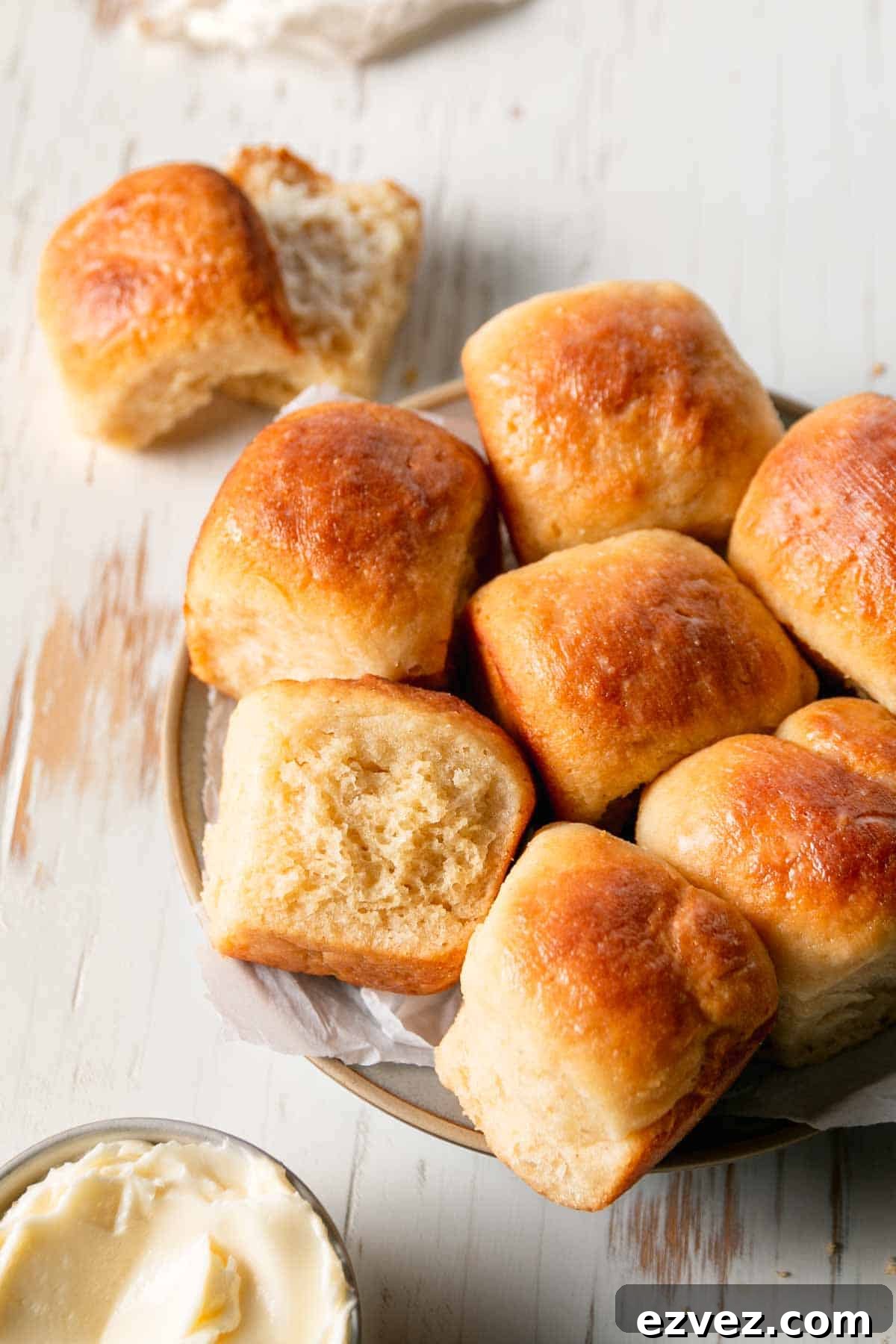 A plate filled with gluten-free hawaian rolls, one on its side to show texture and the another split open and spread with butter. 