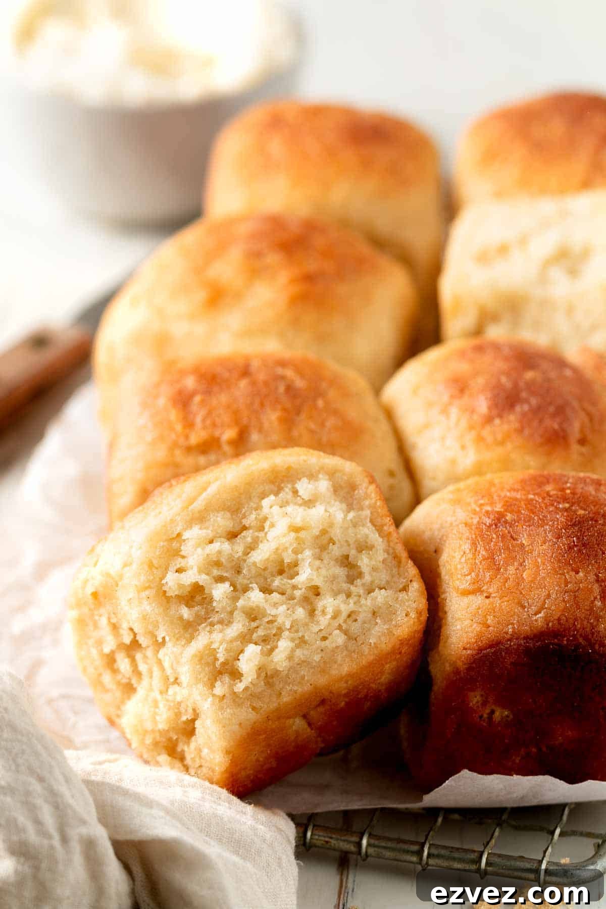 Gluten-free Hawaiian Rolls rest on parchment paper, on a wire rack, one on it's side showing soft texture.