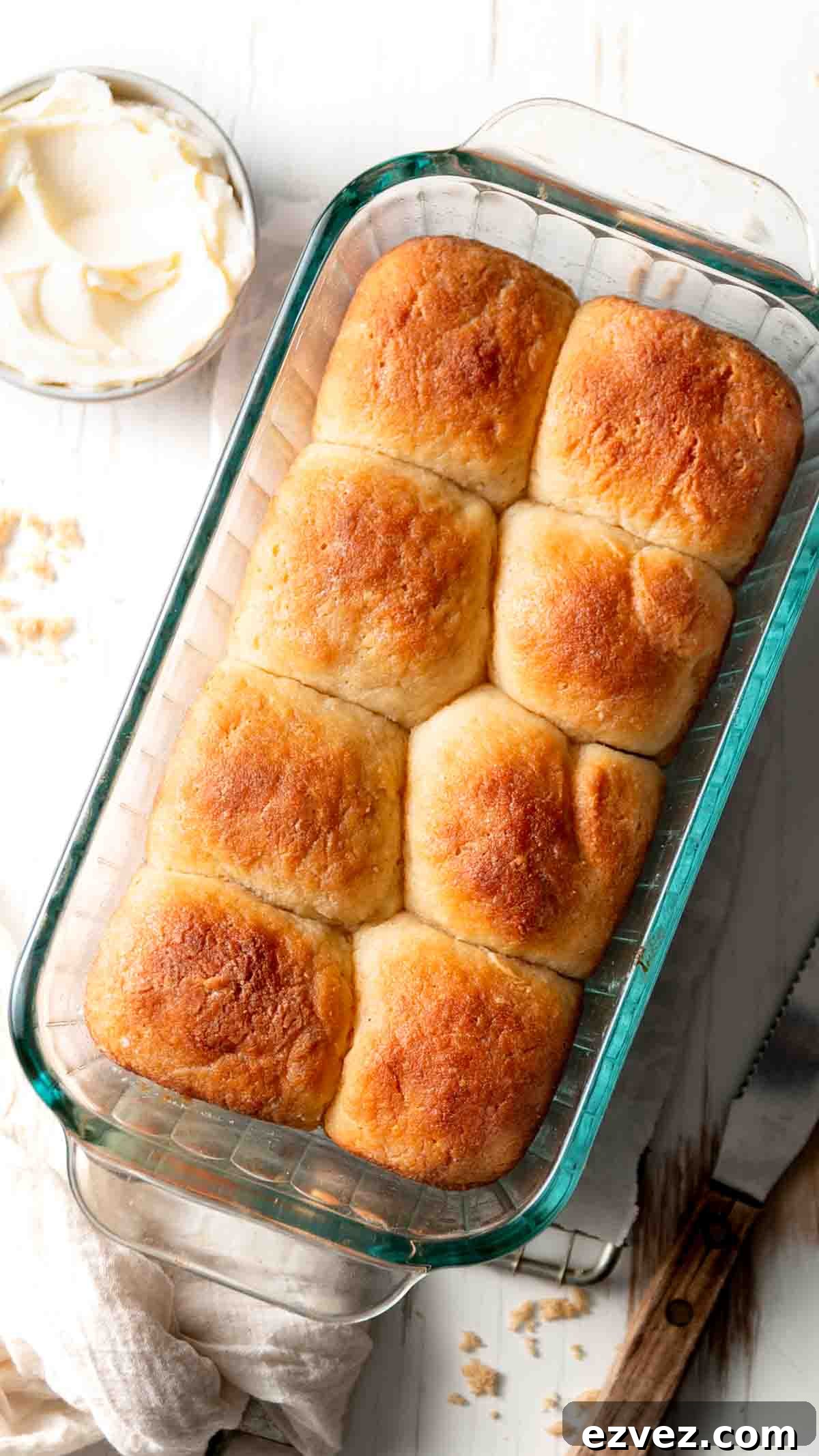 Eight gluten-free Hawaiian rolls in a regular sized pyrex loaf pan next to a bowl of softened butter. 