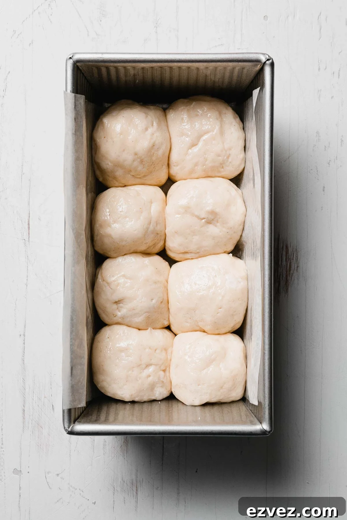 Eight shaped gluten-free roll dough balls placed snugly in a loaf pan, ready to rise.