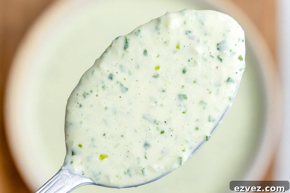 A closeup of a spoonful of green goddess dressing hovering over a bowl.