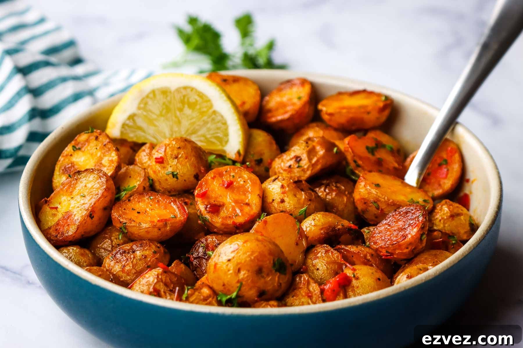 A bowl of roasted harissa potatoes garnished with a lemon wedge.