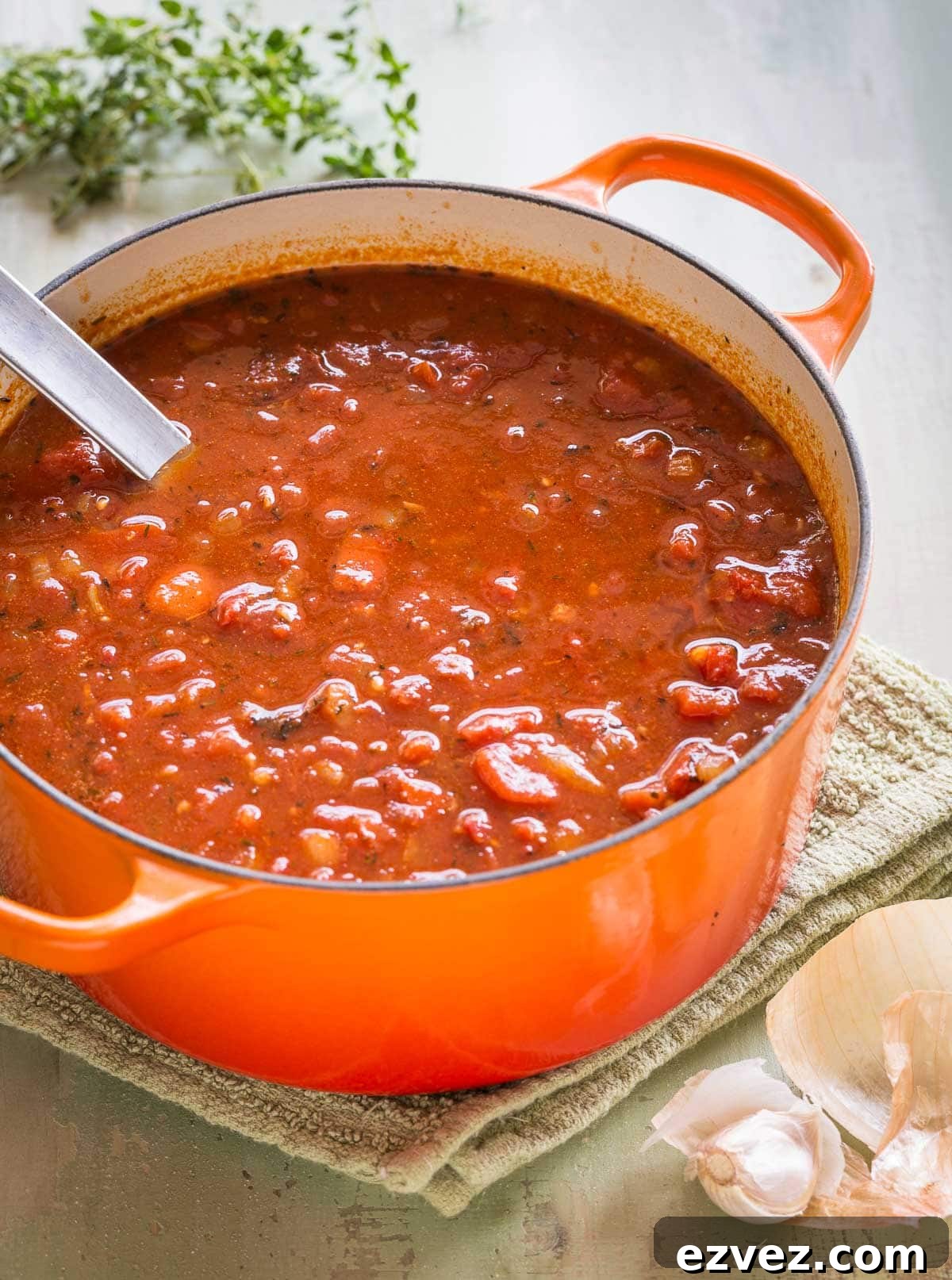 Chunky tomato soup in an orange Dutch oven ready to be pureed, with a silver ladle.