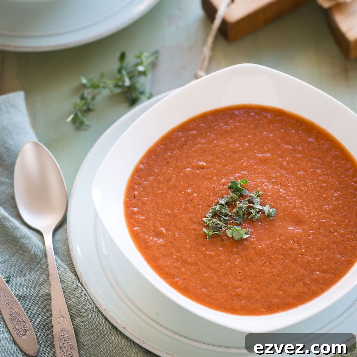 A single bowl of tomato soup with a sprig of fresh thyme leaves and silver spoon.