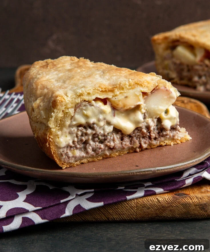 A slice of double crusted cottage pie with ground beef, red potatoes and cheese sauce on a brown plate with purple napkins.