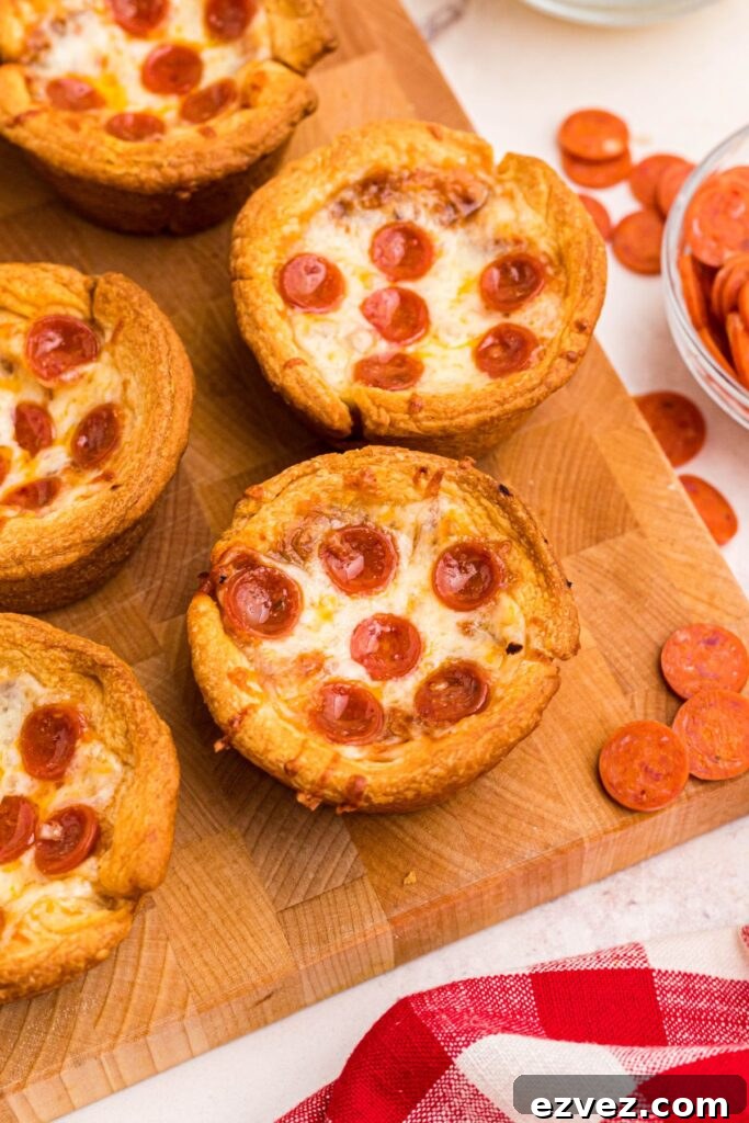 Golden pizza cupcakes on a wooden cutting board with mini pepperonis scattered around it. 