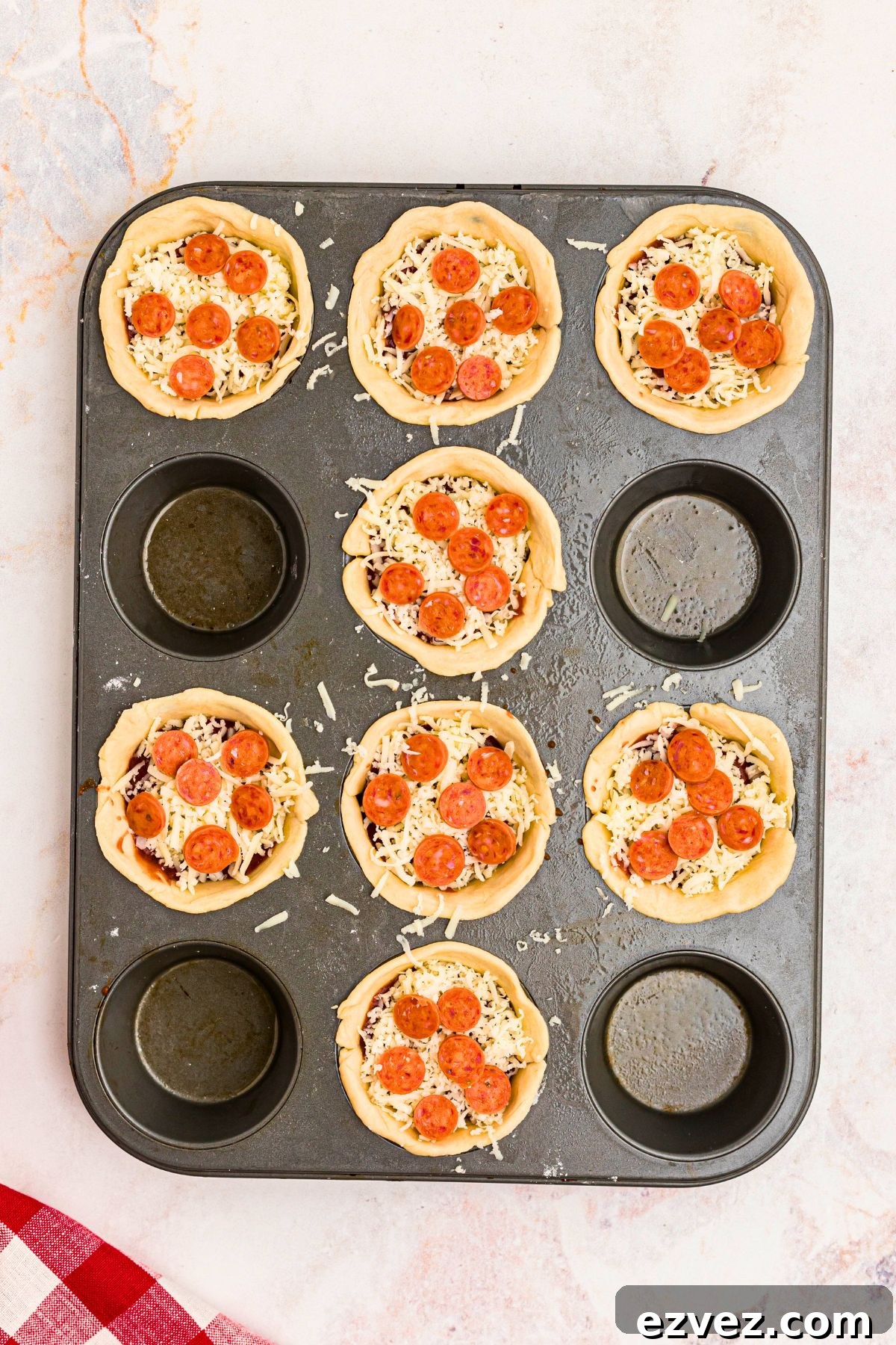 Muffin tin filled with crust dough, sauce, cheese, and pepperoni before being cooked.