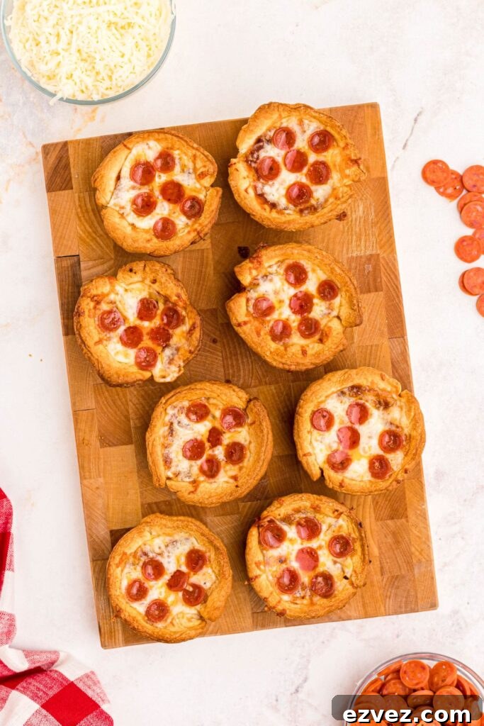 Golden crispy mini pizza cupcakes on a wooden cutting board, with mini pepperonis scattered on a marble table. 