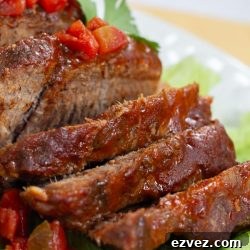 Sliced pot roast with diced tomatoes on top and a red sauce.