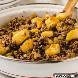 hamburger hash topped with cheddar cheese in a skillet with a wooden spoon