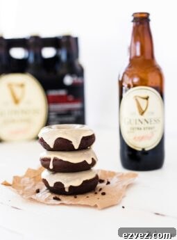 guinness chocolate donuts with bottle of stout beer, stack of three glazed chocolate donuts on brown paper with white wood table