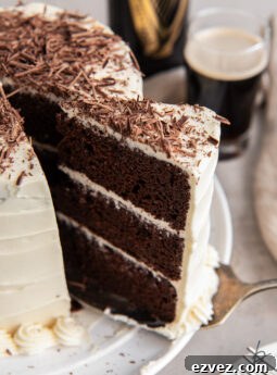 three layer chocolate guinness cake slice being pulled away from cake with baileys frosting and chocolate shavings.