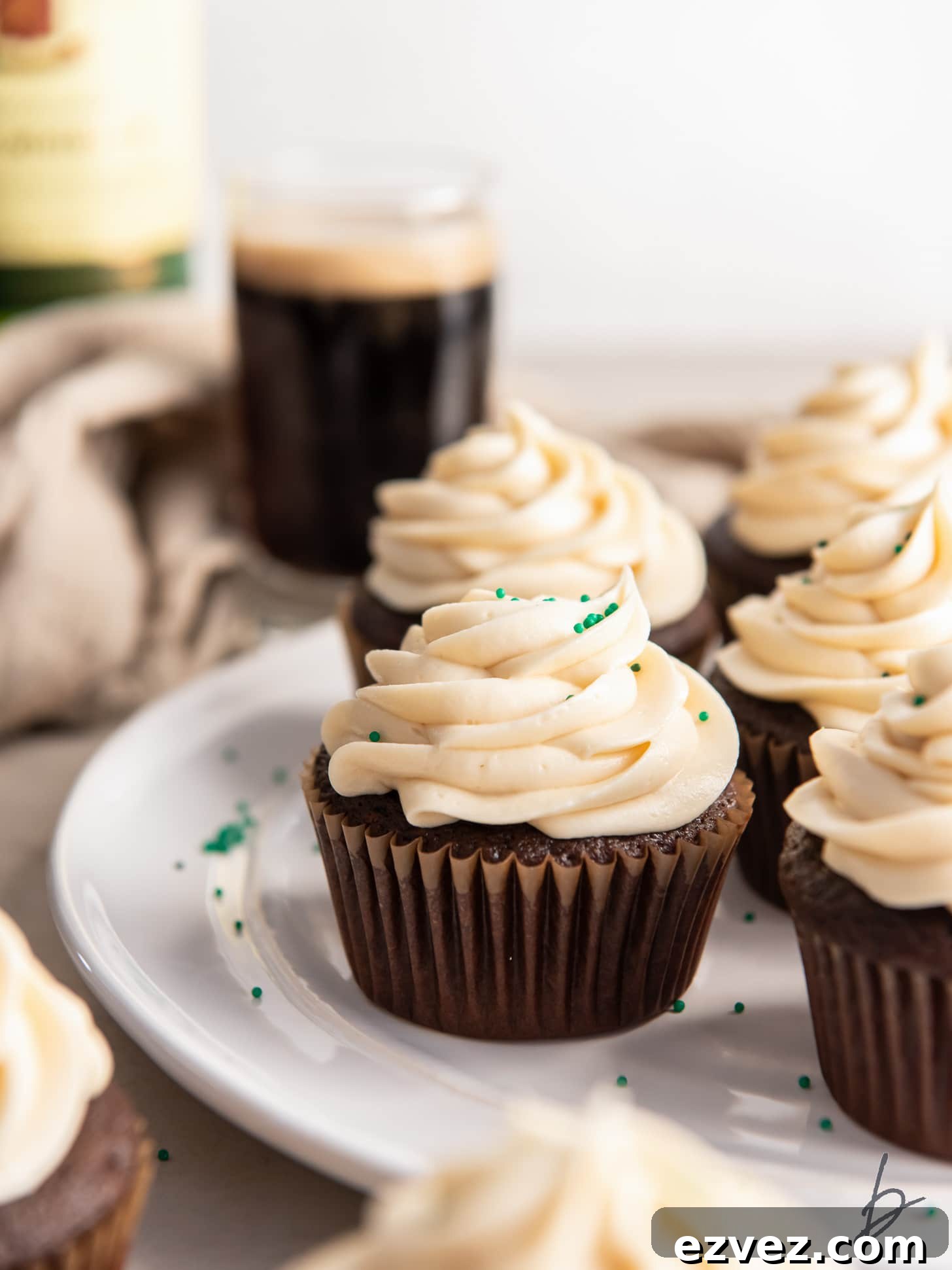 guinness cupcakes with baileys frosting on a plate with a few green sprinkles.