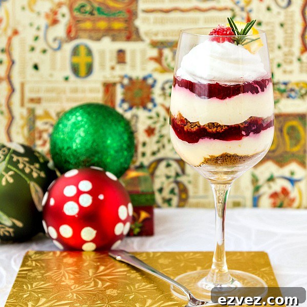 A wine glass layered with orange cheesecake mix, cranberry orange jam, and gingersnap crumbles. Christmas decorations in the background.