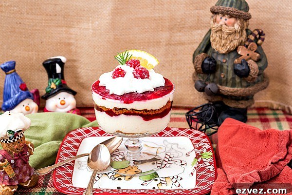 An individual trifle dish with cheesecake parfait on a table with holiday decorations.