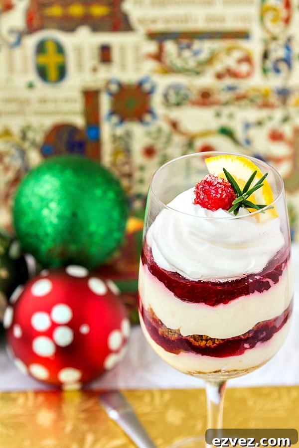 A wine glass of dessert topped with whipped cream, a sugared cranberry, and a small sprig of rosemary.