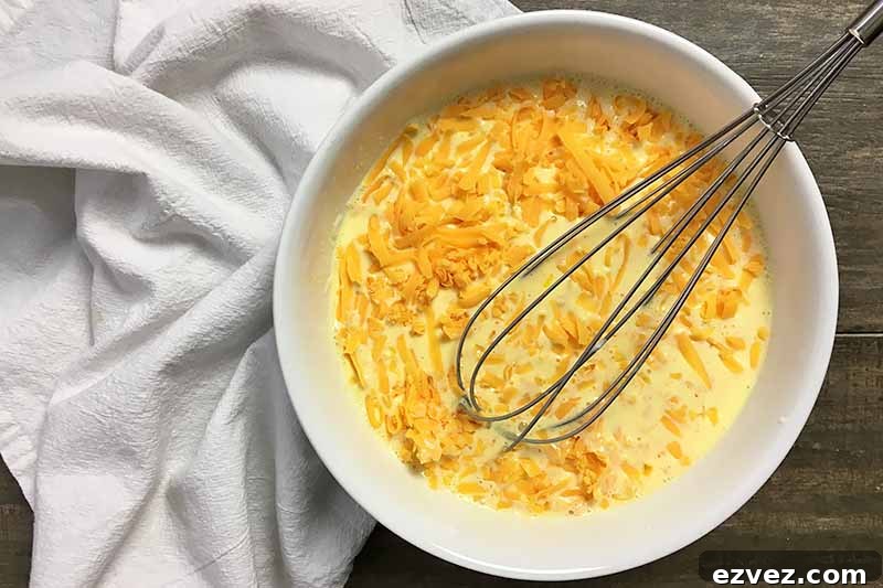 Horizontal image of an egg and cheese mixture in a bowl with a whisk.