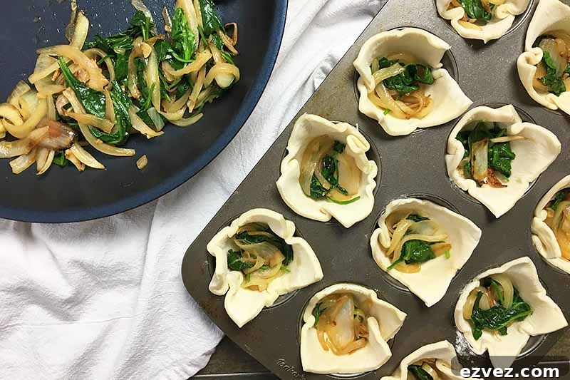 Horizontal image of a spinach mixture in the bottom of dough-lined muffin tins.