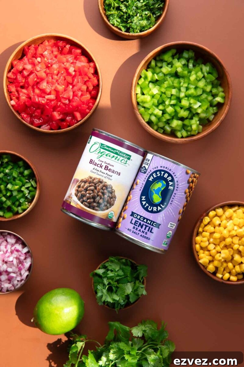 lentil cowboy caviar ingredients in bowls: chopped tomatoes, diced bell peppers, chopped cilantro, diced jalapenos, diced onion, corn kernels, canned black beans, canned lentils, fresh lime, bunch of cilantro
