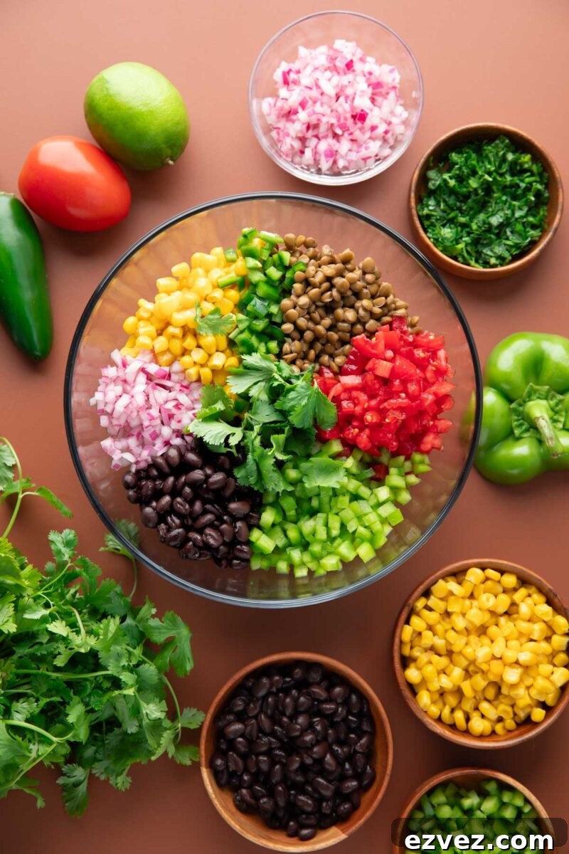 glass mixing bowl with cowboy caviar ingredients surrounded by additional ingredients in small bowls