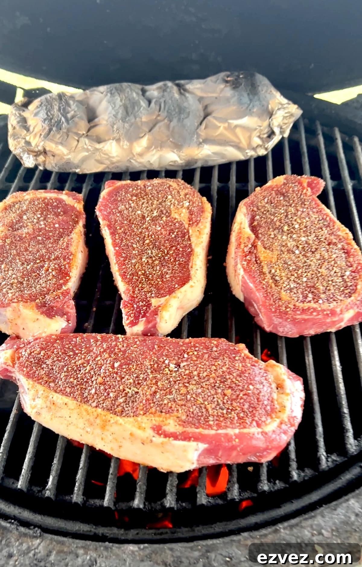 Grilling ribeye steaks with foil packet of potatoes.