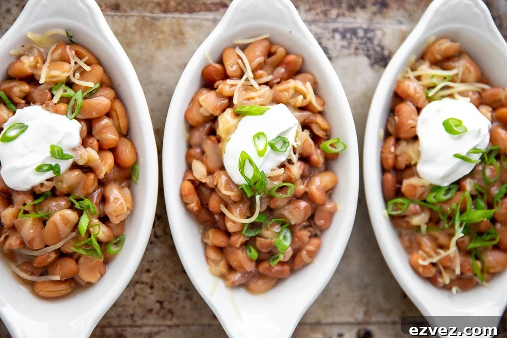 Three serving dishes of Instant Pot pinto beans topped with cheese and sour cream.