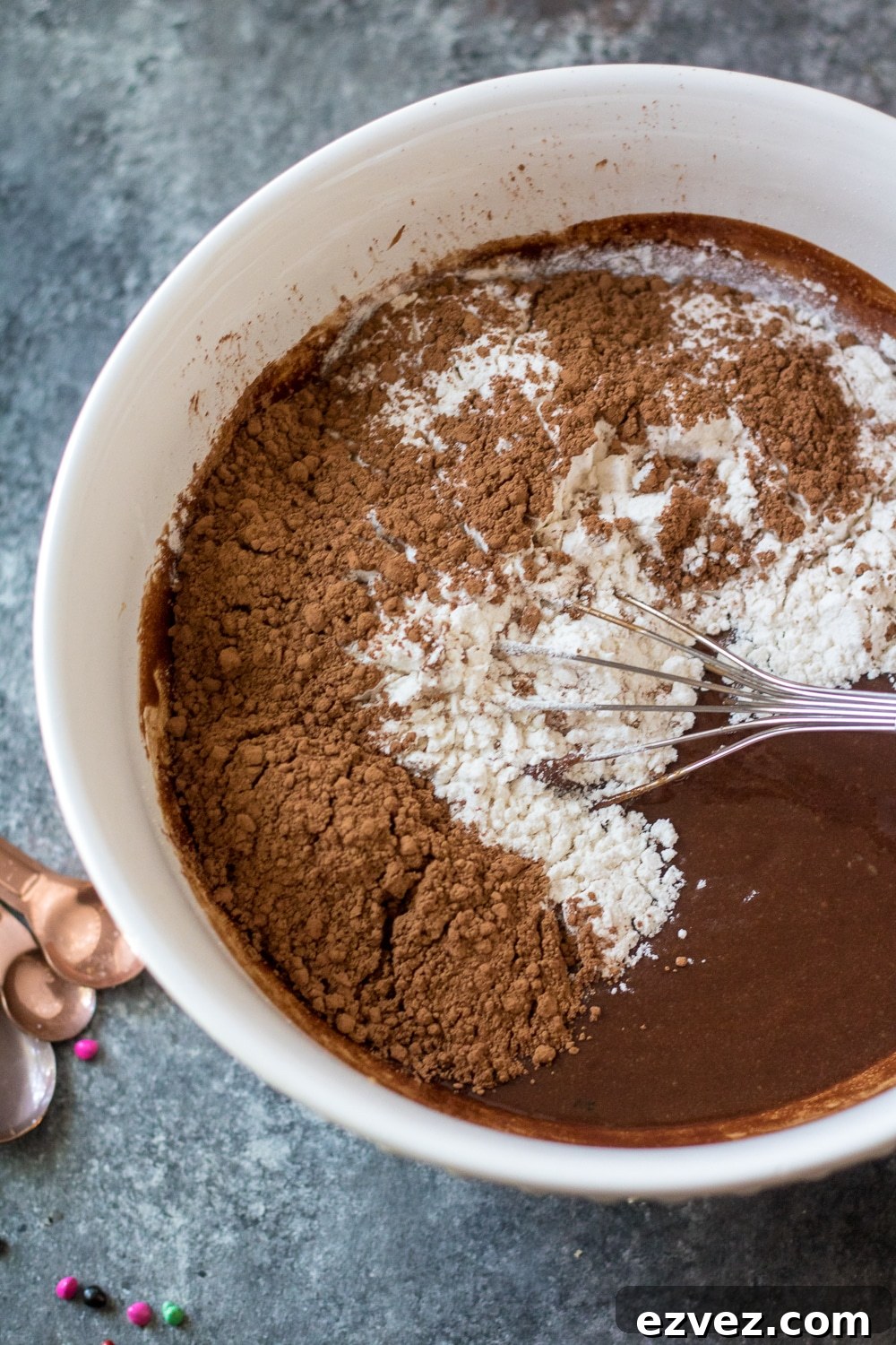 Cosmic Brownies Recipe — Fudgy, No-Bake Chocolate Squares 6 flour and cocoa powder being added to a white bowl of brownie batter