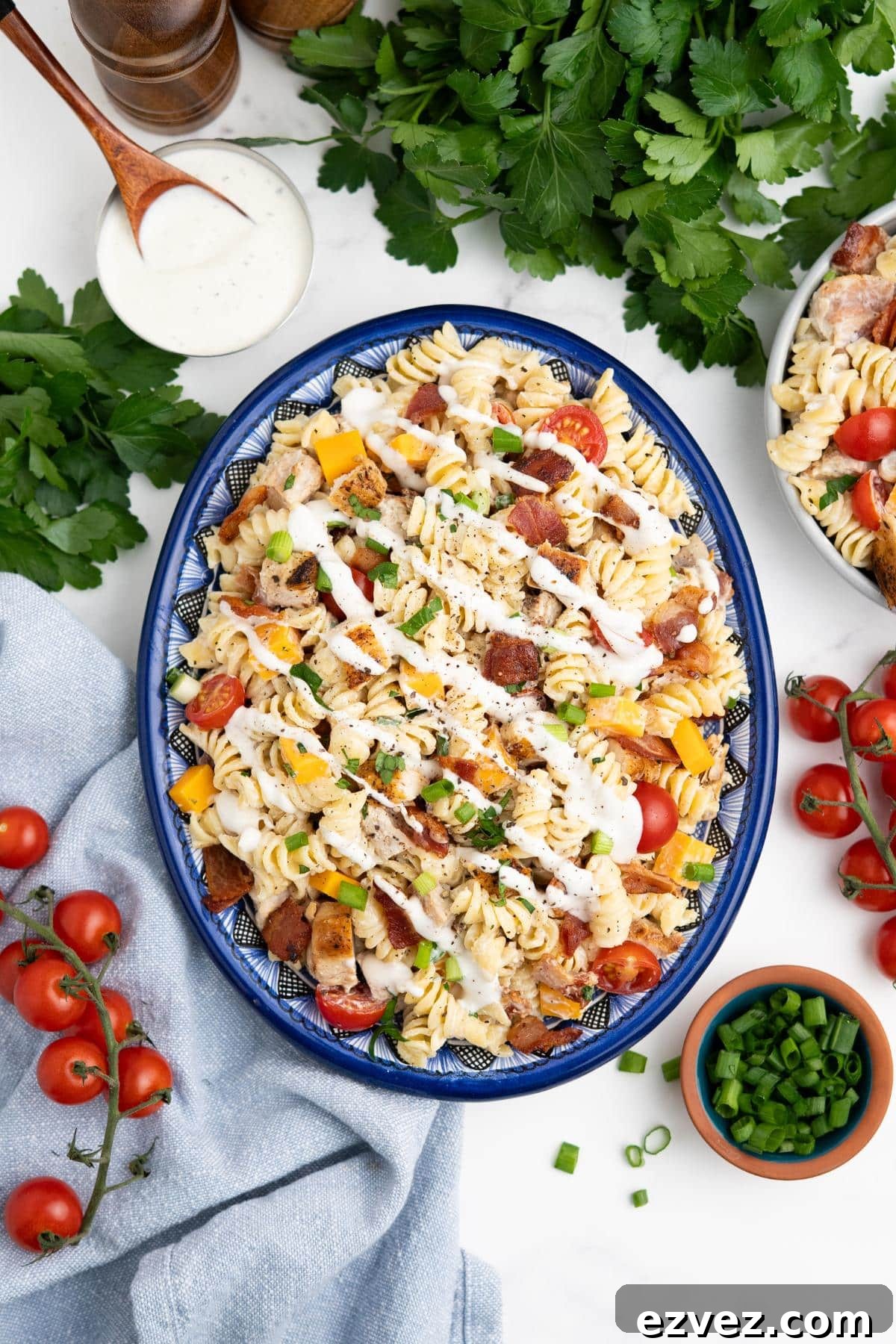 A platter of chicken bacon ranch pasta salad on a table with fresh vegetables scattered around.