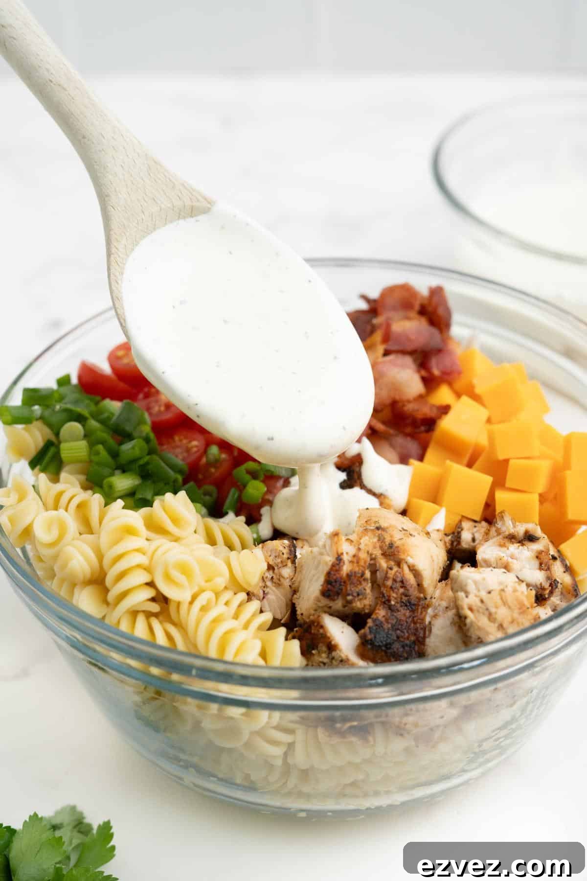A spoon drizzling the dressing over the pasta salad.