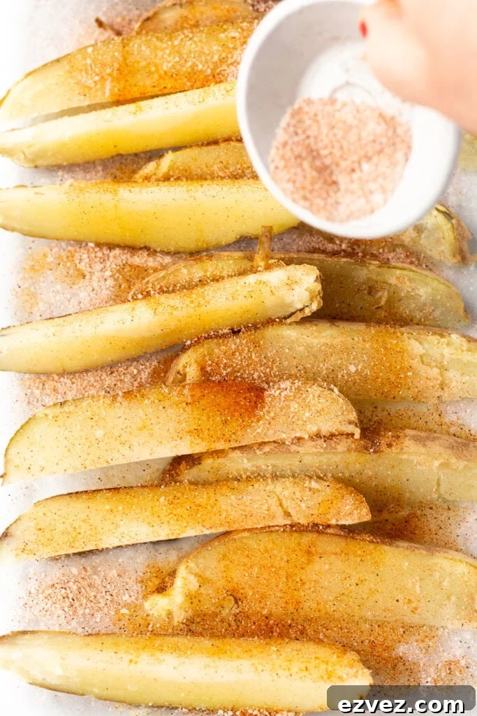 seasoning being poured over large russet potato wedges in a large glass dish.