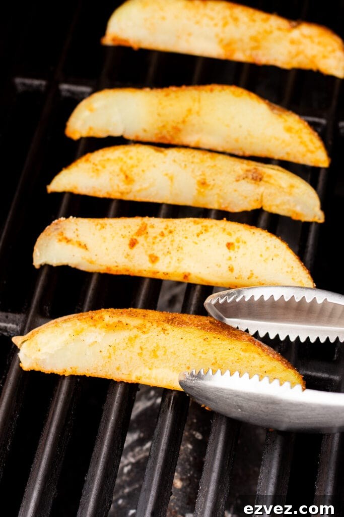 par cooked russet potato wedges being place on a hot grill with a pair of silver tongs.