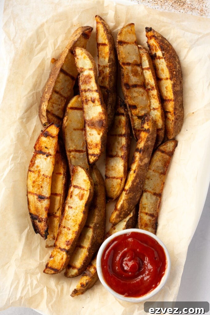 top down shot of grilled potato wedges on top of brown parchment paper with a small white bowl of ketchup in the lower part of the frame.