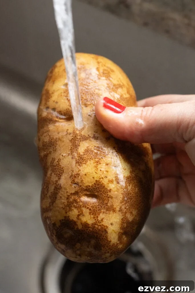 Close up of a russet potato being washed under a sink faucet.