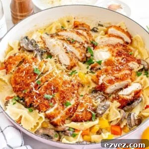 A plate of bow tie pasta topped with breaded, sliced Cajun chicken, mushrooms, diced bell peppers, and grated cheese, served in a large white dish with a pepper grinder and seasonings nearby—a true Cheesecake Factory copycat.