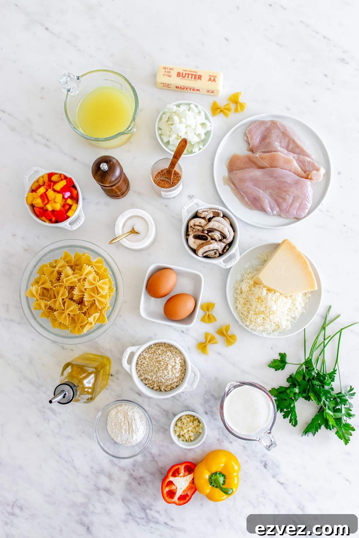 Ingredients arranged on a marble surface, including chicken breasts, pasta, cheese, vegetables, spices, eggs, butter, and cooking oil for a Louisiana Cajun Chicken Pasta Cheesecake Factory copycat.