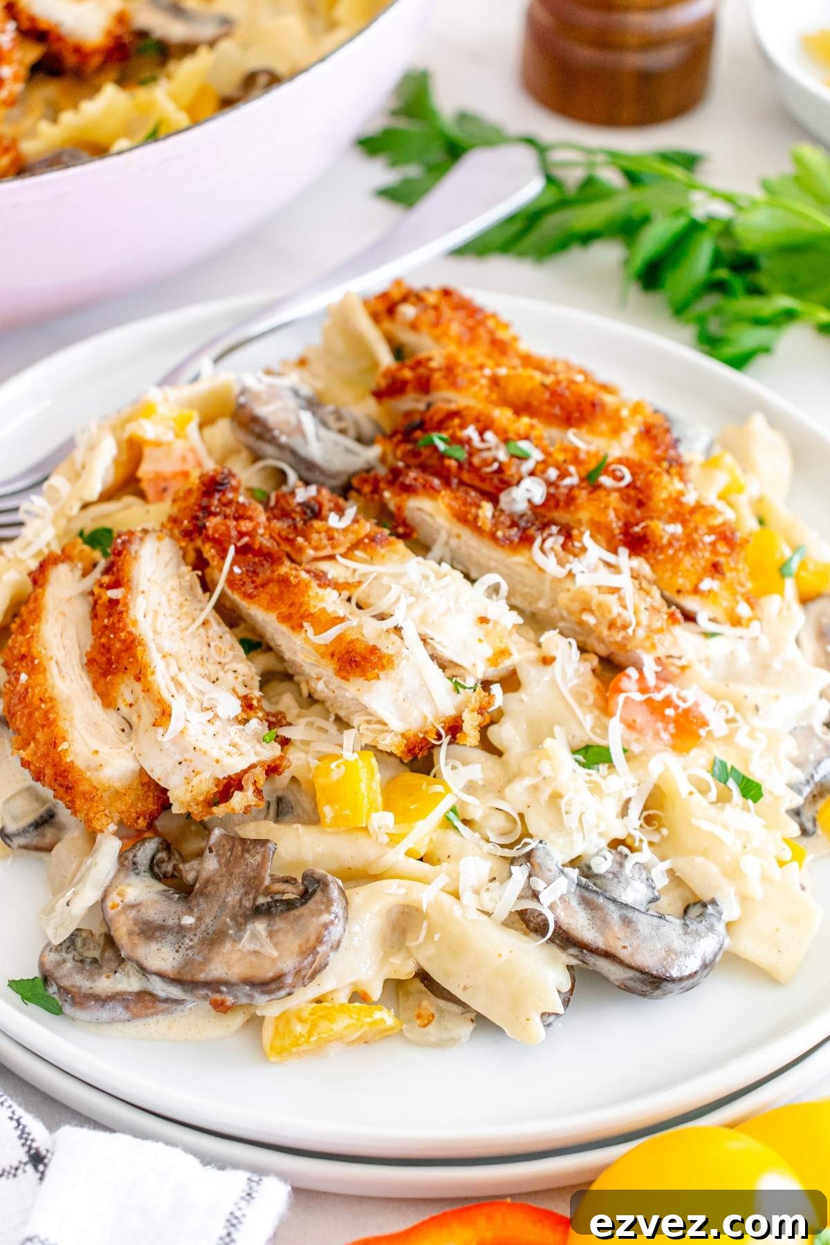 A plate of creamy bow tie pasta with mushrooms, bell peppers, and grated cheese, topped with breaded and sliced Louisiana Cajun chicken breast, inspired by a Cheesecake Factory copycat recipe.