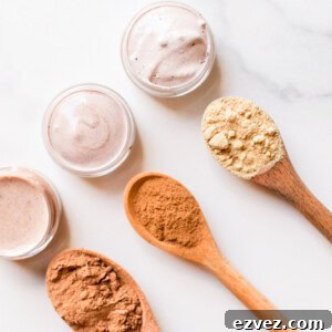 Top 3 best natural concealer recipes in small glass containers with the different color pigments in wooden spoons.