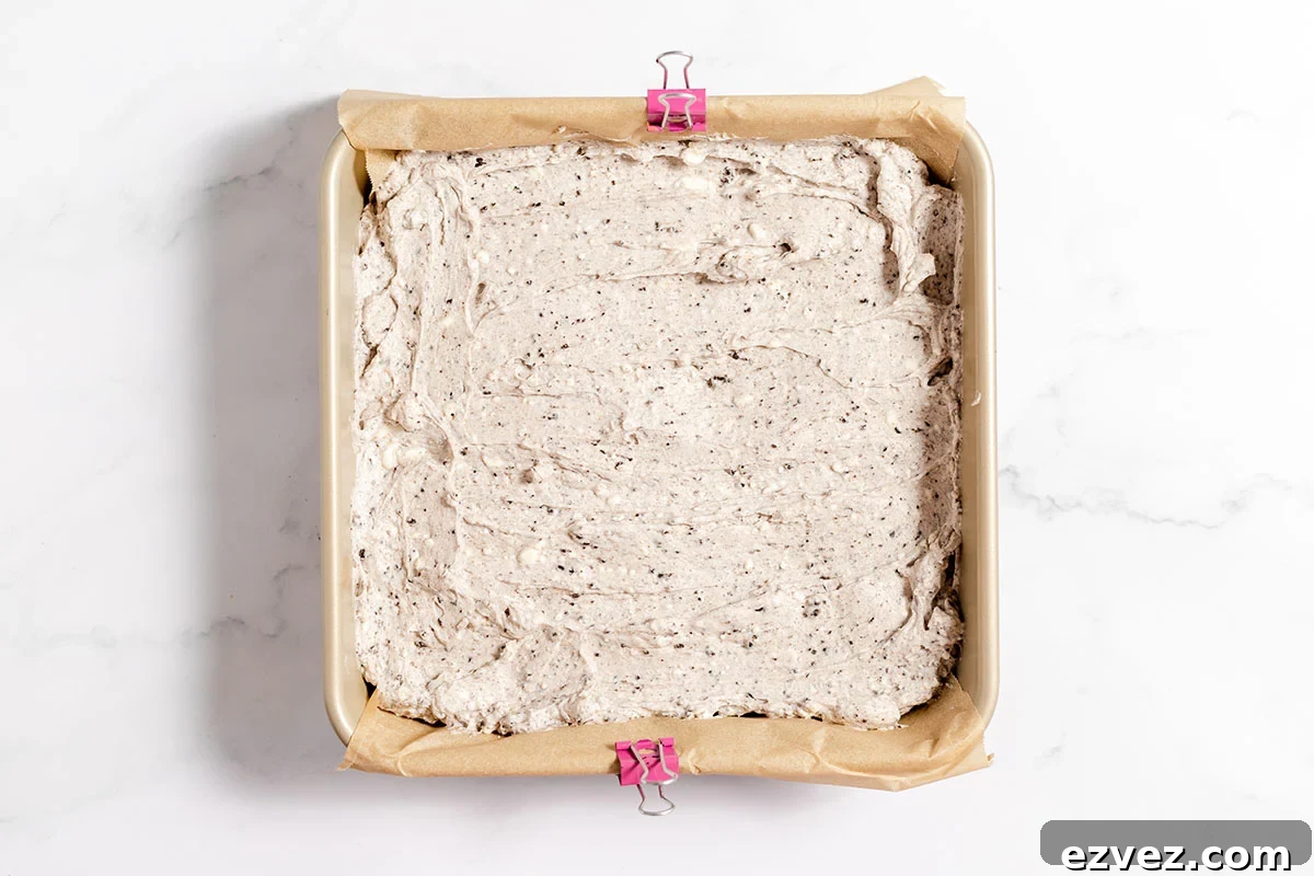 Cookies & Cream Brownies Recipe — Fudgy Oreo-Stuffed Brownies 14 Baked Cookies and cream brownies in a parchment-lined baking pan with a creamy Oreo topping.
