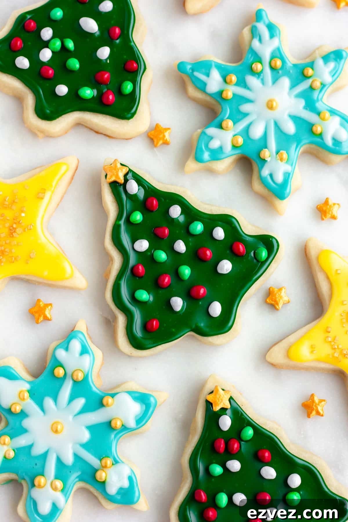 lots of vegan sugar cookies on a white marble background decorated with various colors and sprinkles and shapes