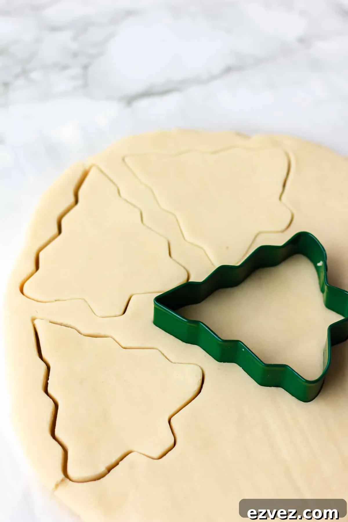 cutting tree shapes out of sugar cookie dough on marble backdrop