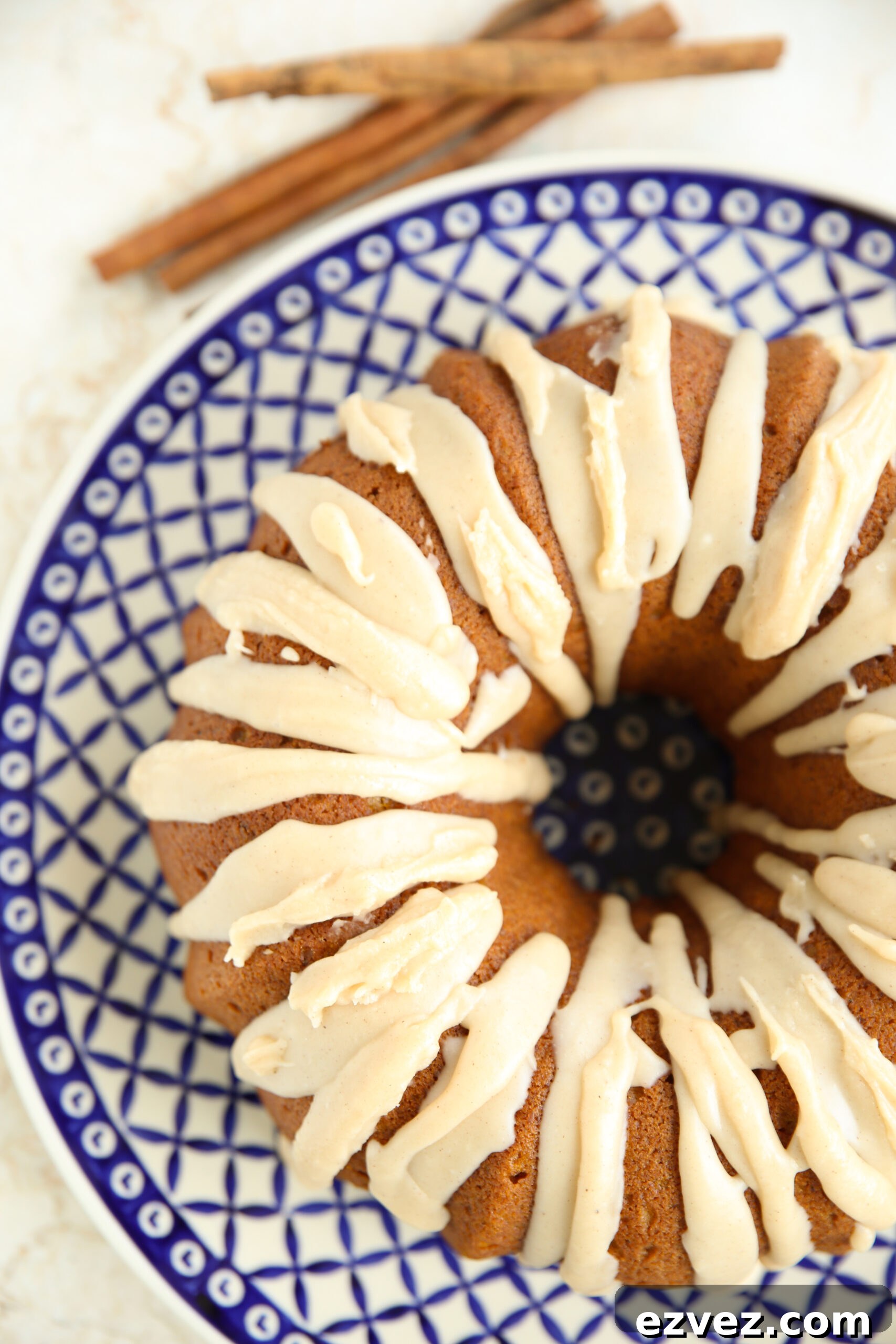 Pumpkin Spiced Bundt Cake with Brown Butter Icing on a large Polish pottery plate. Faded in the top background are a few cinnamon sticks.