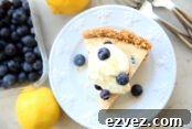 In the background are a couple of lemons, two forks, and a container of blueberries. There's a white dessert plate with a slice of lemon blueberry pie topped with whipped cream, candied lemon zest and a few blueberries. On each side of the slice of pie is a single blueberry.
