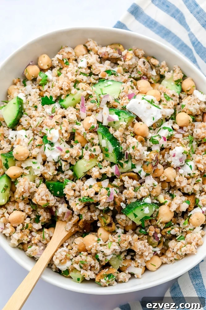 close up photo of a bowl of grain salad with wooden spoon and blue striped towel