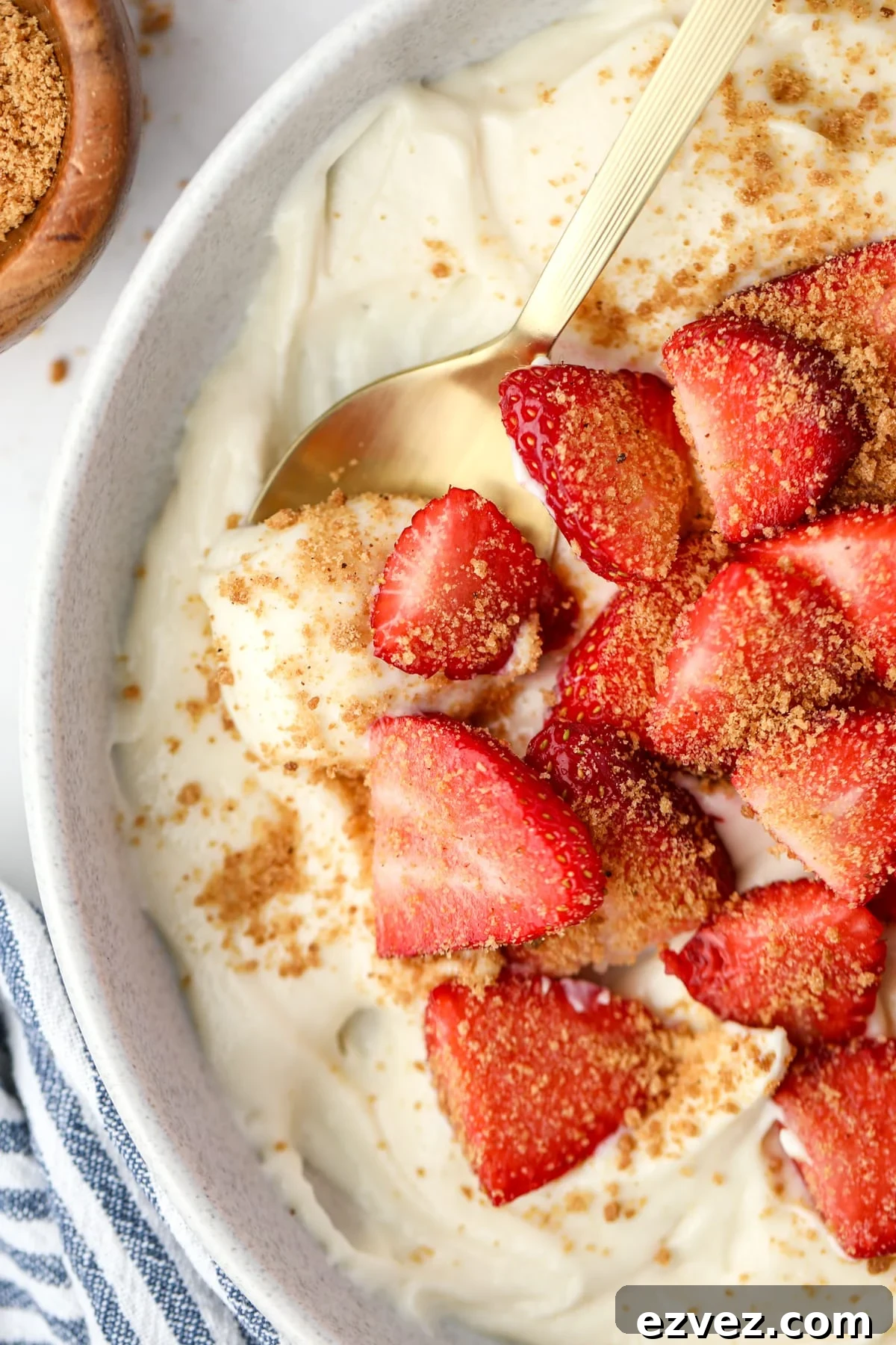 A spoon taking a portion of yogurt from a bowl topped with strawberries.