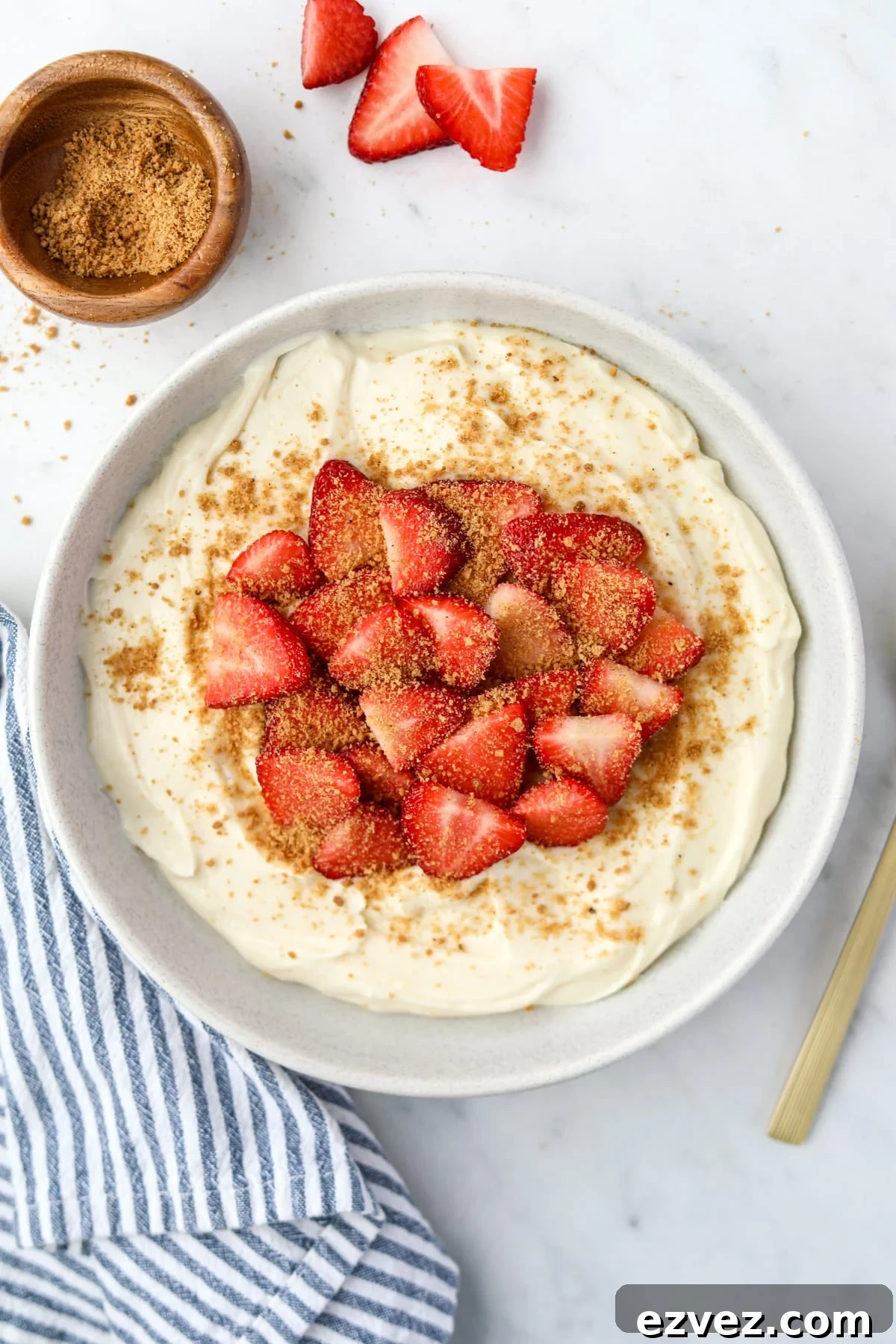 A bowl of yogurt topped with strawberries and graham cracker crumbs.