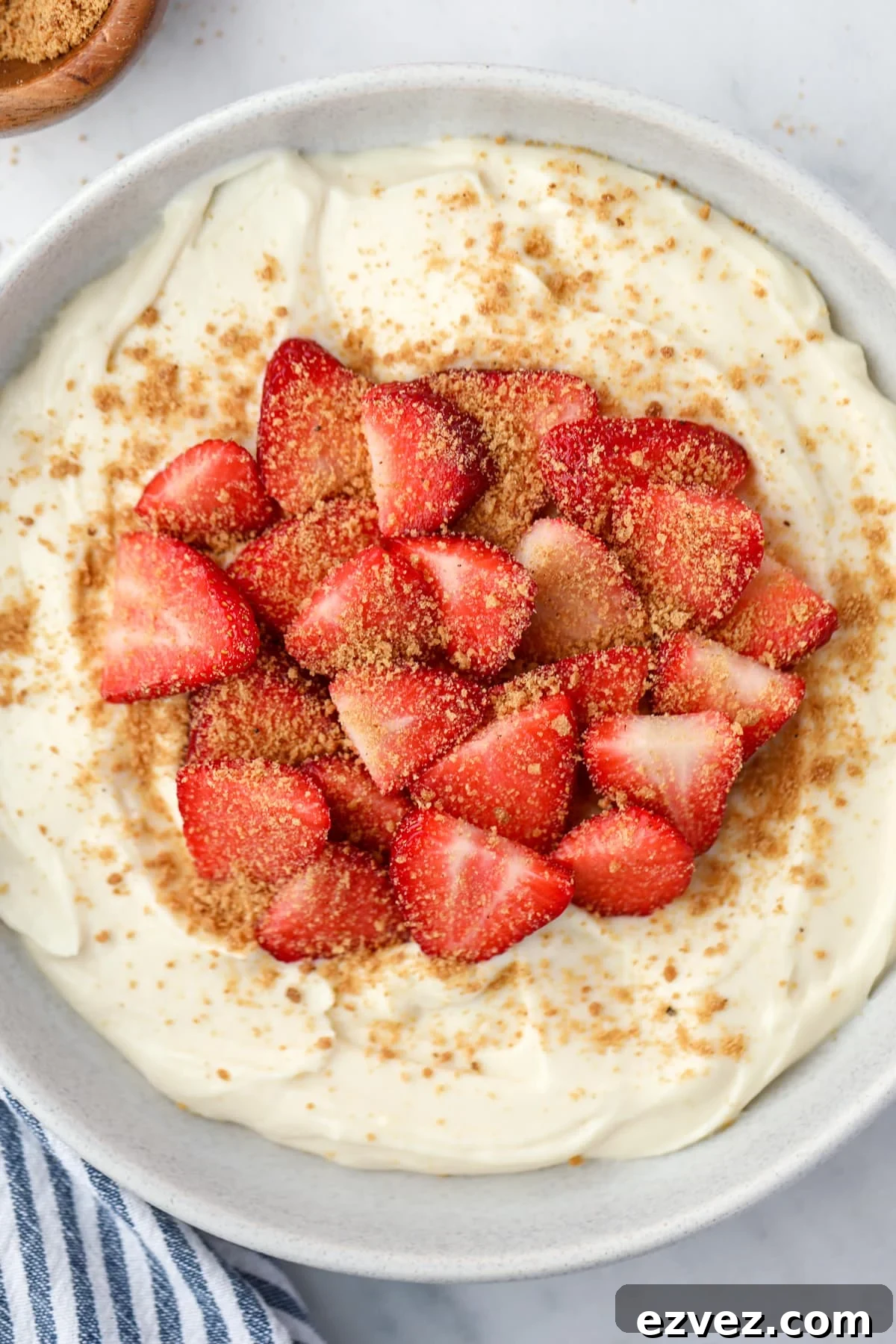 A bowl filled with yogurt, fresh strawberries, and graham cracker crumbs.