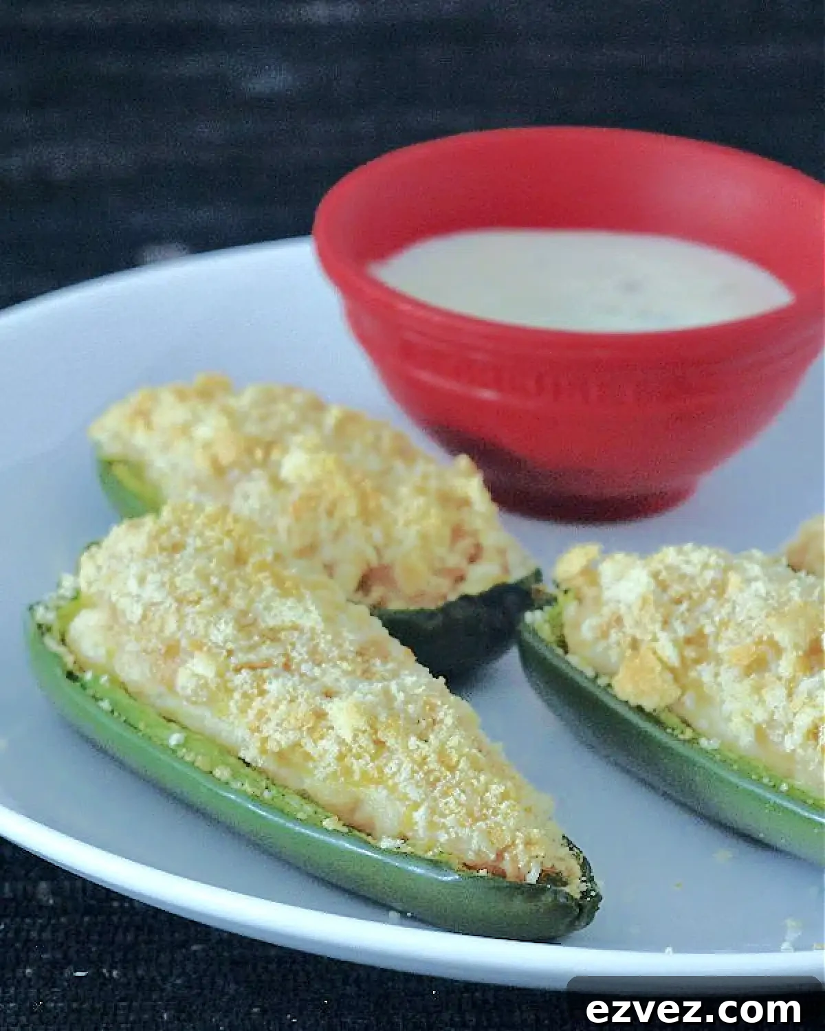 close up of Pineapple Jalapeño Poppers on a white plate with a small red bowl of ranch dressing on the side.